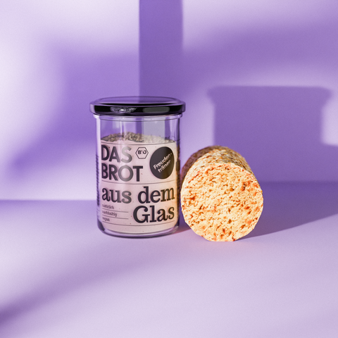 Glas mit Brotbackmischung "Das Brot aus dem Glas" und angeschnittenem Brotlaib. Bio, nachhaltig und vegan für frisches Brot zuhause.
