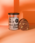 Brotbackmischung "Das Brot aus dem Glas" im Glas mit angeschnittenem Brotlaib. Enthält Zutaten wie Zimt und Dinkelmehl. Nachhaltig und vegan.